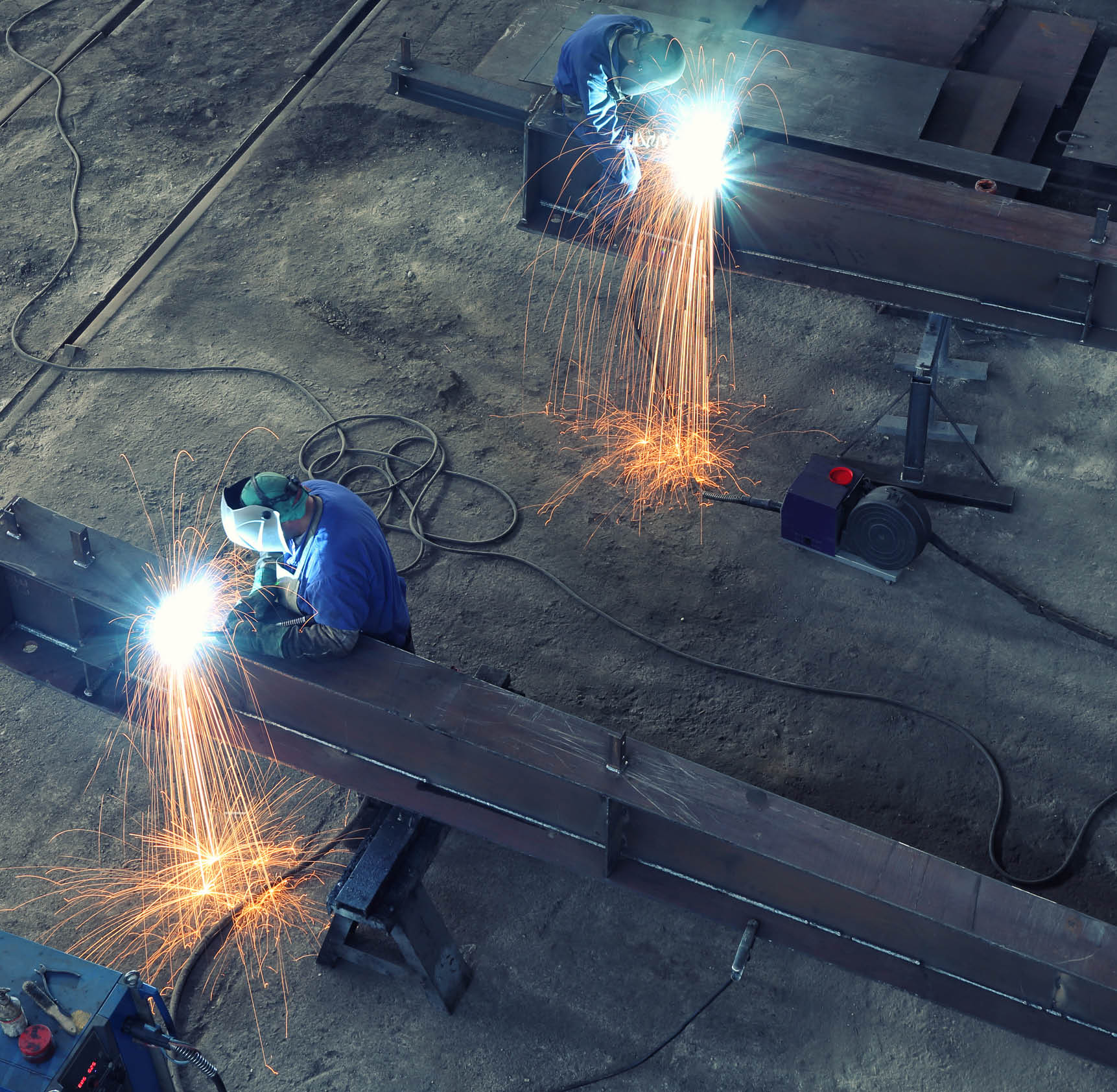 Workers with protective mask welding large steel beam, view from above. Workers can not be recognized because of the masks and equipment . 